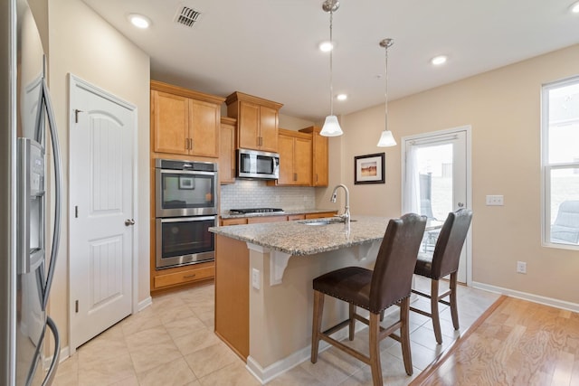 kitchen with visible vents, a kitchen island with sink, a sink, stainless steel appliances, and decorative backsplash