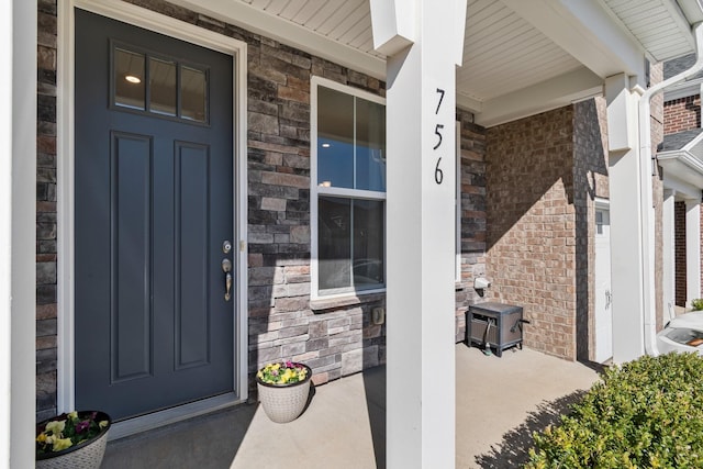 property entrance featuring brick siding, covered porch, and stone siding