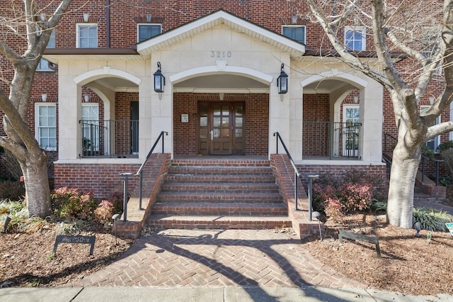 view of exterior entry with brick siding and a porch