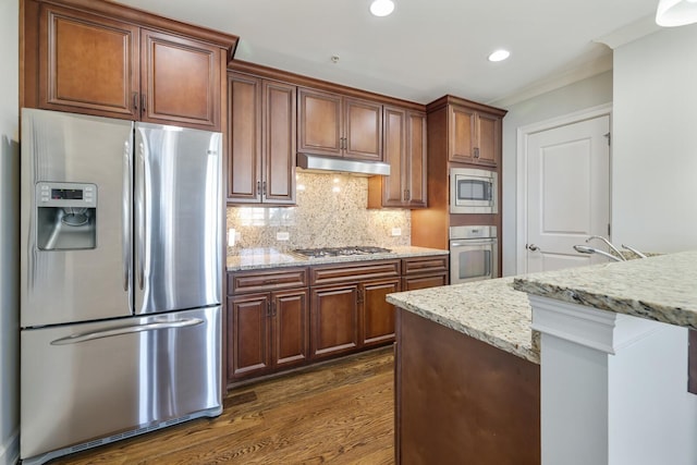 kitchen featuring tasteful backsplash, under cabinet range hood, light stone counters, appliances with stainless steel finishes, and dark wood-style flooring