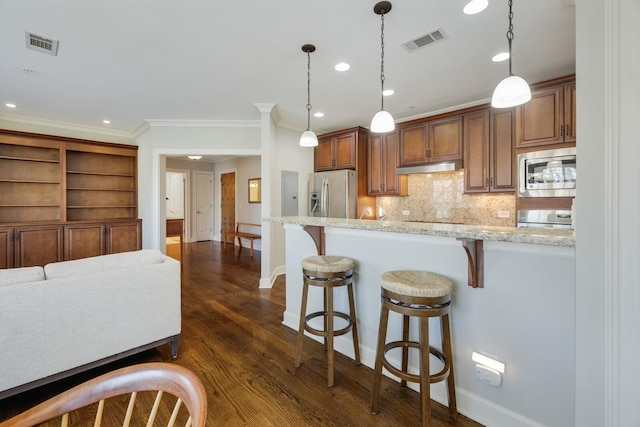 kitchen featuring under cabinet range hood, visible vents, stainless steel appliances, and a breakfast bar