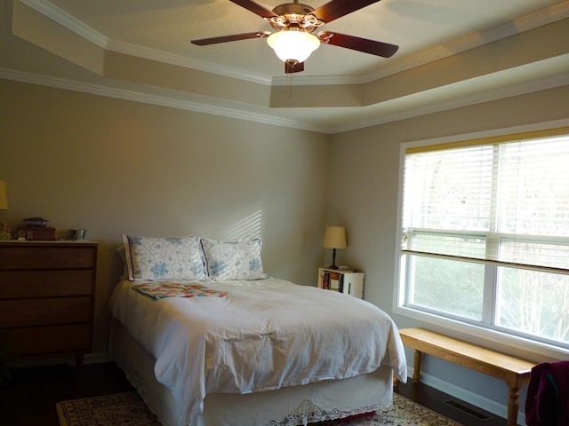 bedroom with visible vents, ceiling fan, a tray ceiling, ornamental molding, and dark wood-style floors