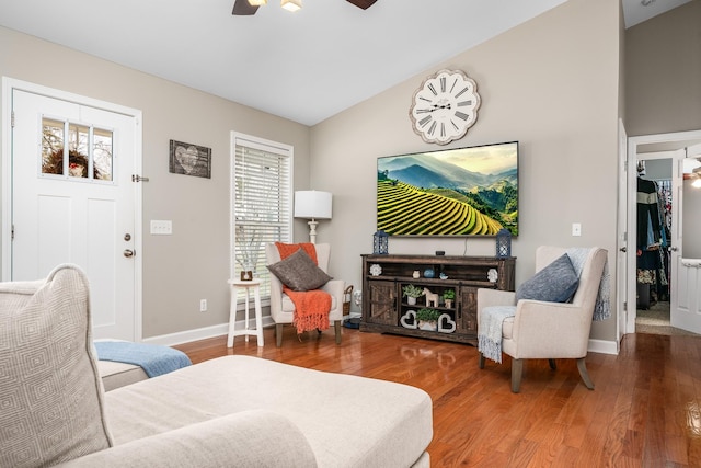 living area featuring ceiling fan, wood finished floors, baseboards, and vaulted ceiling