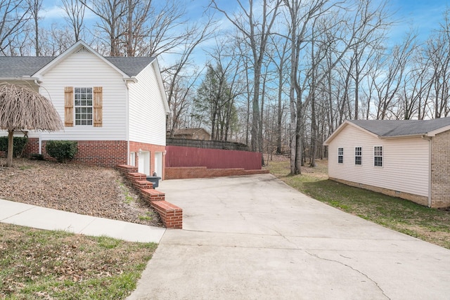 view of home's exterior featuring an attached garage, fence, brick siding, and driveway