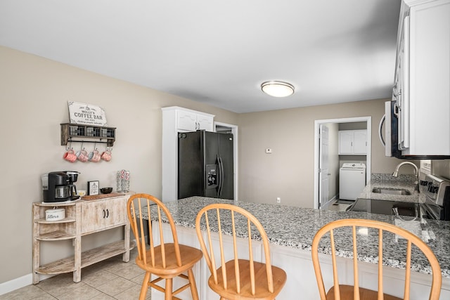 kitchen featuring washer / clothes dryer, a sink, white cabinetry, stainless steel microwave, and black refrigerator with ice dispenser