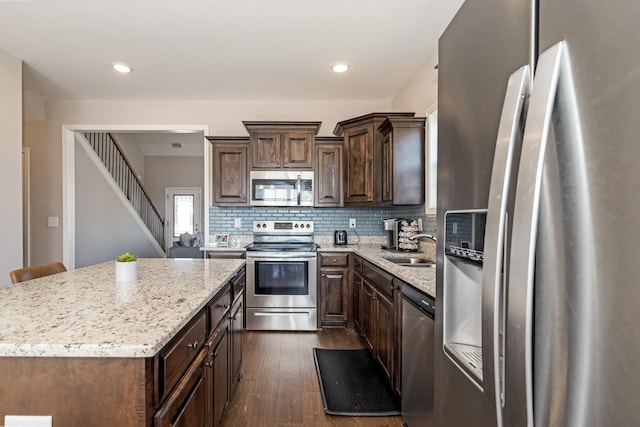 kitchen featuring tasteful backsplash, dark brown cabinets, dark wood-type flooring, stainless steel appliances, and a sink