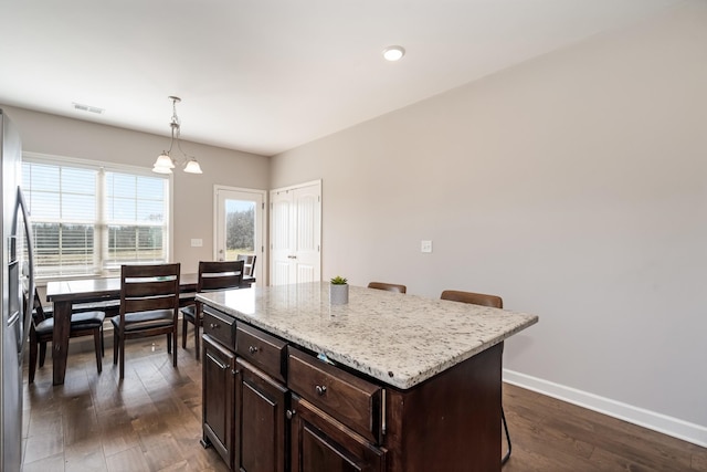 kitchen featuring visible vents, dark wood finished floors, dark brown cabinetry, a breakfast bar area, and baseboards