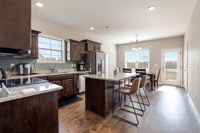 kitchen with a kitchen island, tasteful backsplash, stainless steel appliances, a breakfast bar area, and dark brown cabinets