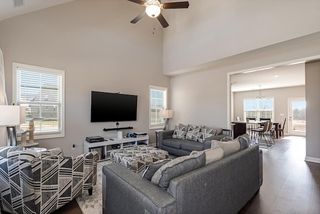 living room with ceiling fan with notable chandelier, a high ceiling, dark wood-style floors, and baseboards