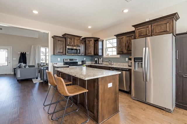 kitchen featuring light wood finished floors, dark brown cabinets, appliances with stainless steel finishes, and a center island