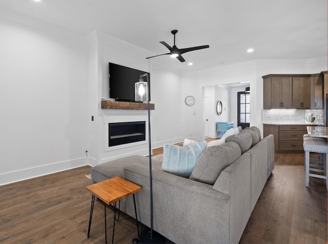 living area featuring ornamental molding, a fireplace, dark wood-style flooring, and baseboards