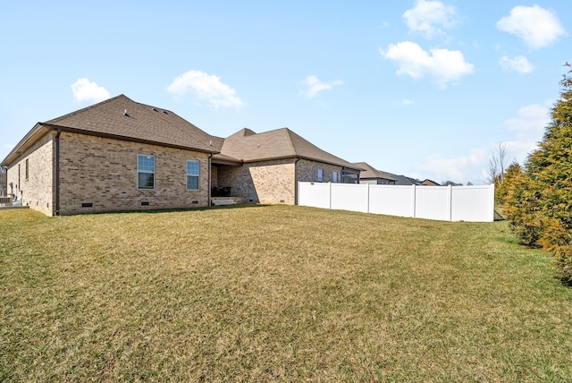 rear view of house featuring fence, a yard, a shingled roof, crawl space, and brick siding