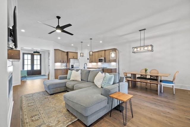 living area with crown molding, baseboards, recessed lighting, ceiling fan with notable chandelier, and light wood-style floors