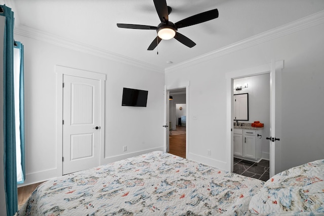 bedroom featuring a ceiling fan, baseboards, ensuite bath, a sink, and crown molding