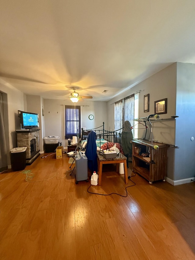 living room featuring baseboards, a stone fireplace, wood finished floors, and a ceiling fan