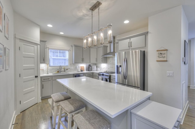 kitchen featuring gray cabinetry, a sink, a center island, stainless steel appliances, and light wood finished floors