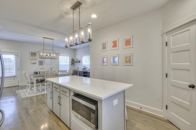 kitchen featuring light wood finished floors, stainless steel microwave, a kitchen island, pendant lighting, and light countertops