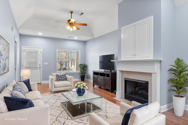 living room featuring light wood-style flooring, baseboards, visible vents, and a tile fireplace