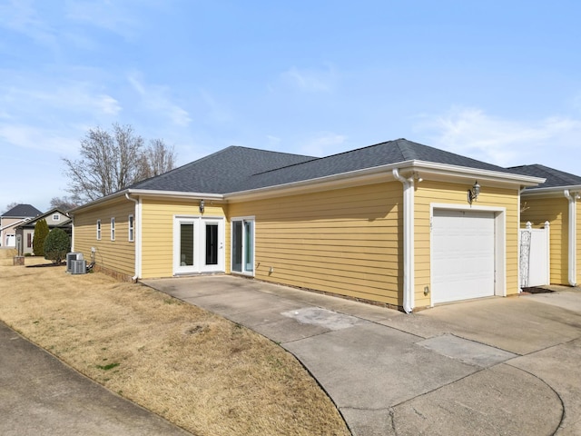 view of front of home featuring concrete driveway, central AC unit, a garage, and a shingled roof