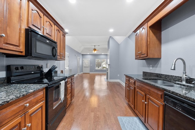 kitchen with black appliances, dark stone counters, brown cabinets, and a sink