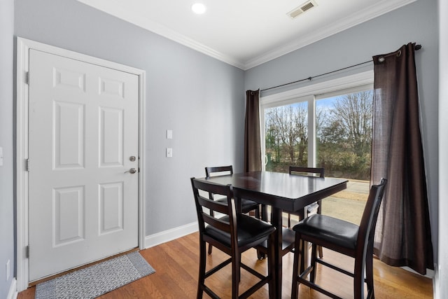 dining room with visible vents, baseboards, wood finished floors, and ornamental molding