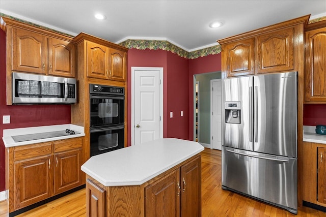 kitchen featuring black appliances, a center island, light wood-style floors, brown cabinetry, and light countertops