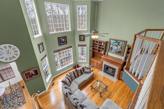 living area featuring light wood-type flooring, a fireplace with flush hearth, visible vents, a high ceiling, and baseboards