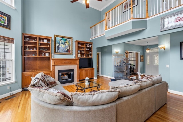 living area with baseboards, a fireplace with flush hearth, wood finished floors, and a ceiling fan