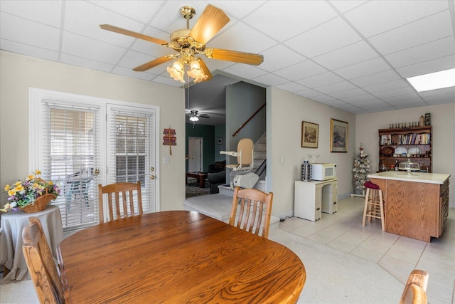 dining area featuring light tile patterned floors, a drop ceiling, ceiling fan, and stairs