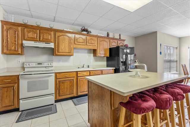 kitchen featuring under cabinet range hood, brown cabinets, black refrigerator with ice dispenser, white electric stove, and a sink