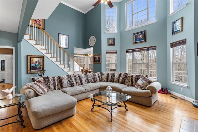 living area with a ceiling fan, wood finished floors, crown molding, baseboards, and stairs