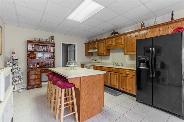 kitchen featuring white appliances, light countertops, a paneled ceiling, under cabinet range hood, and a center island