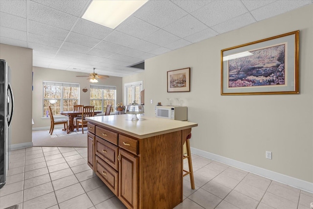 kitchen featuring light tile patterned floors, baseboards, brown cabinets, and a breakfast bar area