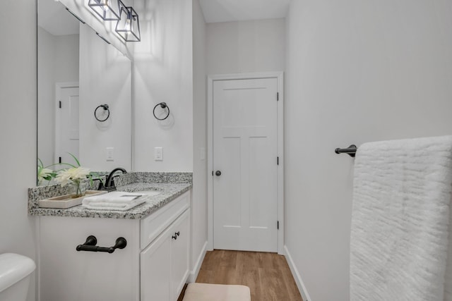 half bathroom with vanity, toilet, wood finished floors, and baseboards