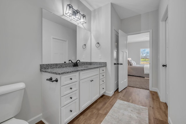 ensuite bathroom with toilet, wood finished floors, baseboards, and ensuite bathroom