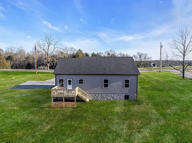 rear view of property with a yard, roof with shingles, and a deck