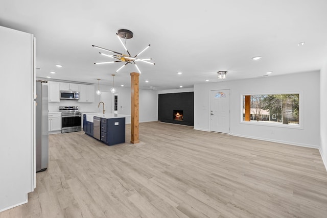 kitchen with open floor plan, light countertops, appliances with stainless steel finishes, white cabinetry, and a sink