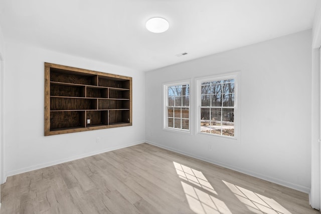 empty room with visible vents, built in features, baseboards, and wood finished floors