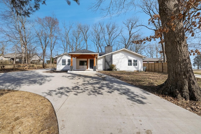 view of front of house featuring driveway, a chimney, and fence