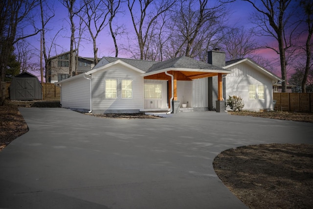 view of front of property with a shed, fence, an outdoor structure, concrete driveway, and a chimney