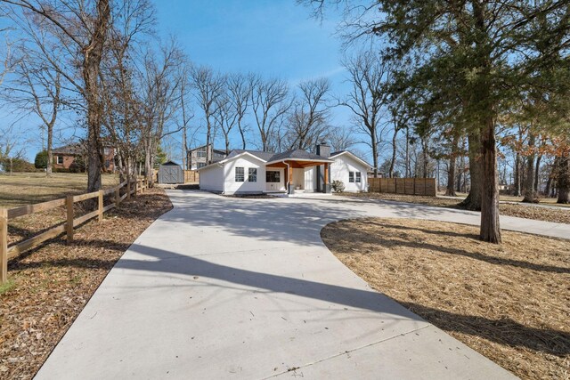 single story home featuring curved driveway, an outdoor structure, a chimney, and fence