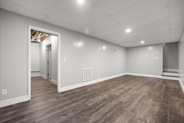 finished basement featuring visible vents, a paneled ceiling, baseboards, and dark wood-style flooring