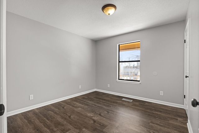 spare room featuring visible vents, baseboards, dark wood-type flooring, and a textured ceiling