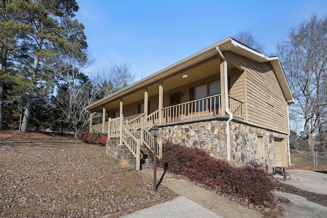 view of front of property featuring driveway, a porch, stairs, a garage, and stone siding