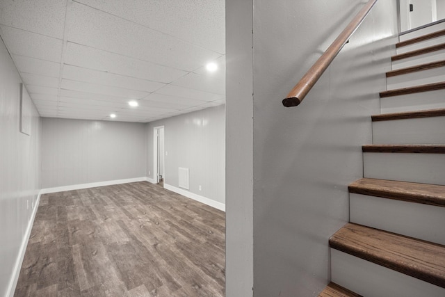 finished below grade area featuring visible vents, baseboards, stairway, wood finished floors, and a paneled ceiling