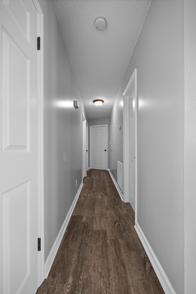 hall featuring wood finished floors, baseboards, and a textured ceiling