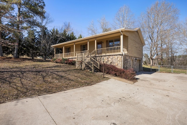 ranch-style house featuring an attached garage, stairway, covered porch, stone siding, and driveway