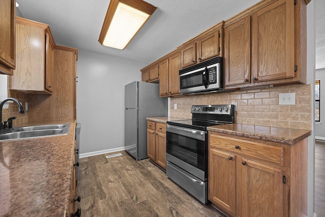 kitchen featuring dark wood-type flooring, baseboards, decorative backsplash, appliances with stainless steel finishes, and a sink