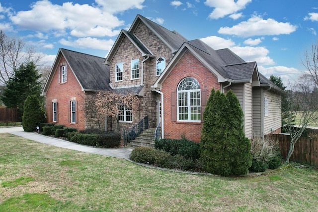 view of front of home with a front yard, fence, brick siding, and stone siding