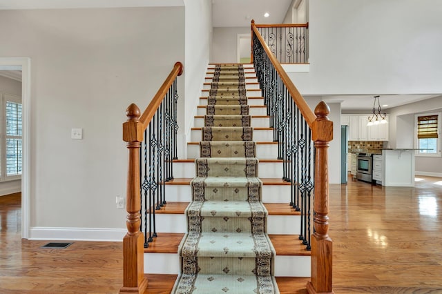 stairway with visible vents, wood finished floors, recessed lighting, a high ceiling, and baseboards